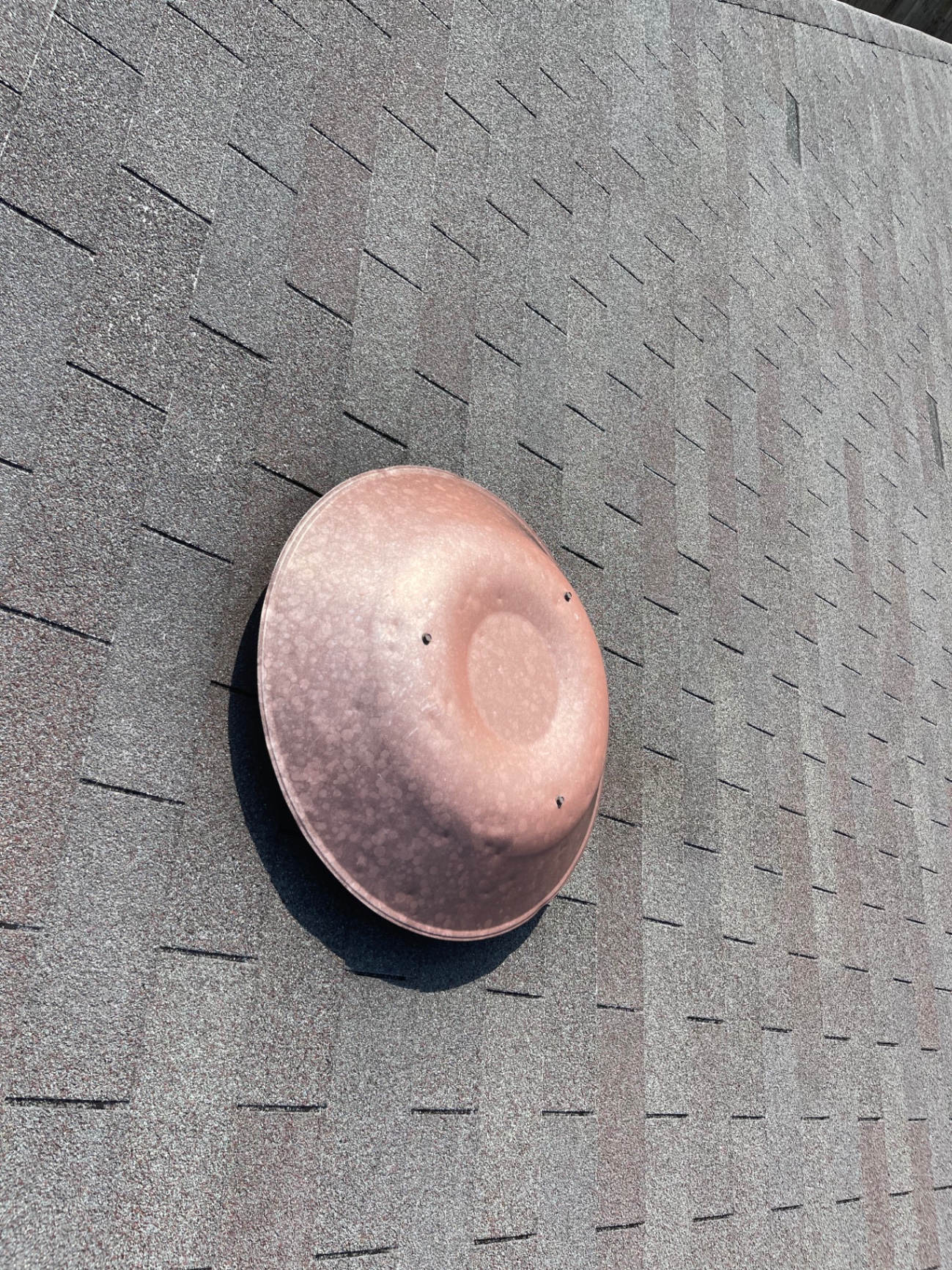 Close-up of a rounded copper roof vent flashing installed through asphalt shingles
