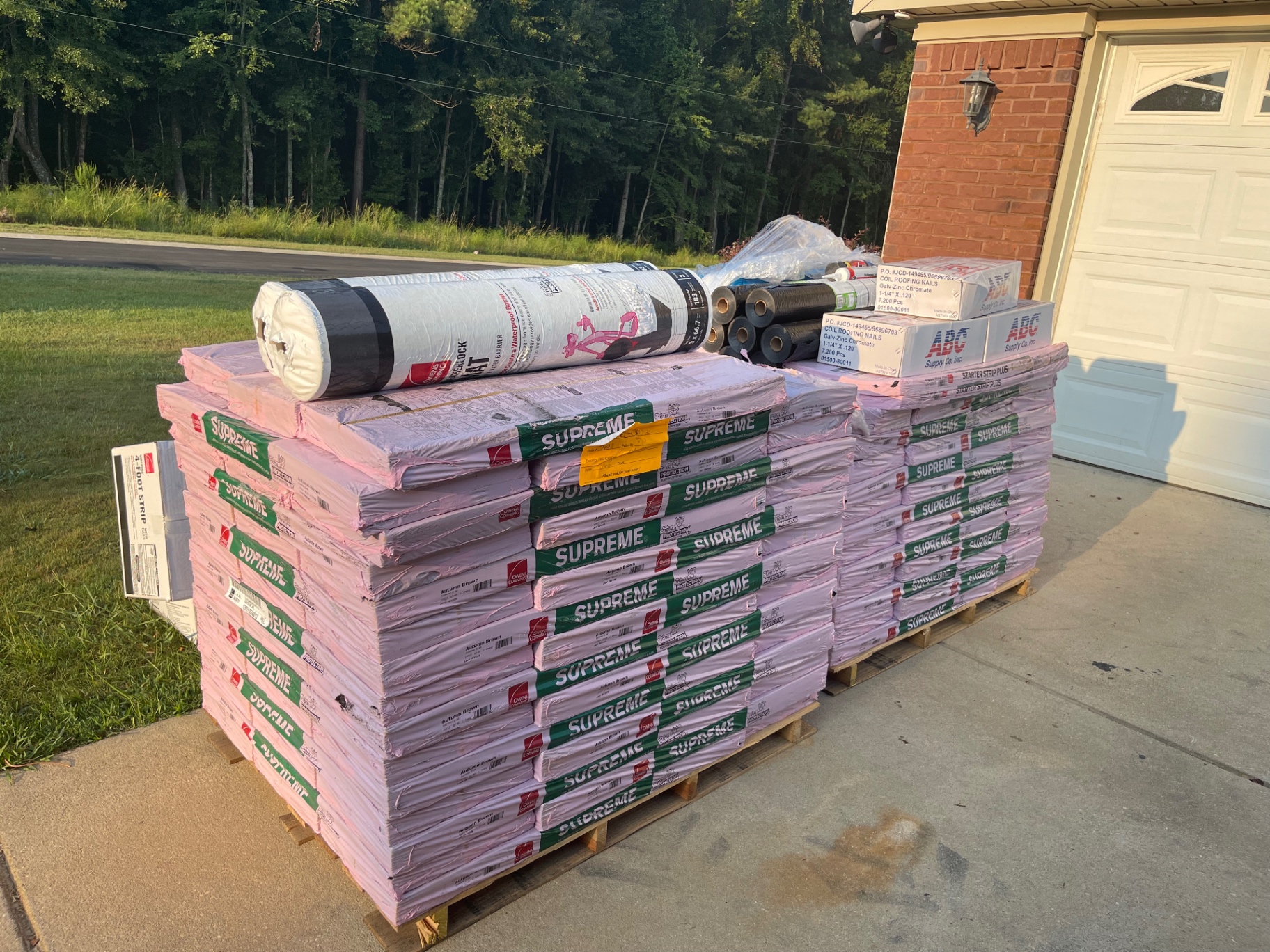 Pallets of shingles, underlayment, and roofing supplies staged neatly at a jobsite before a roof replacement