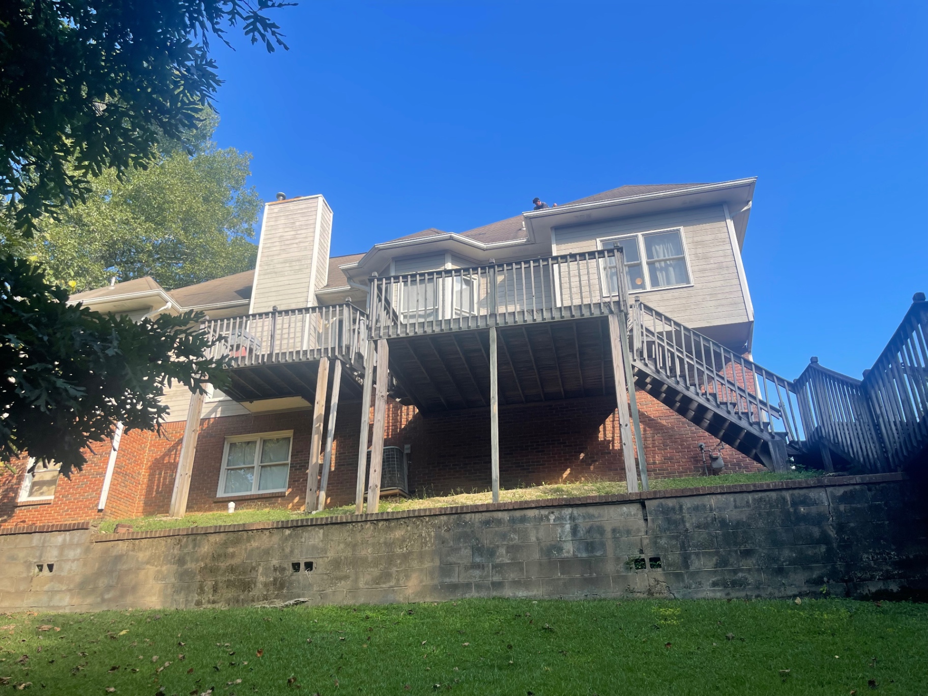 Rear elevation view of a home showing active roof work above a raised deck