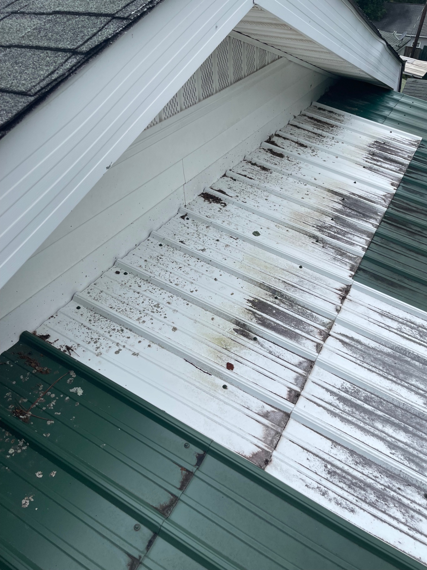 White metal roof section showing staining and debris buildup near a wall transition