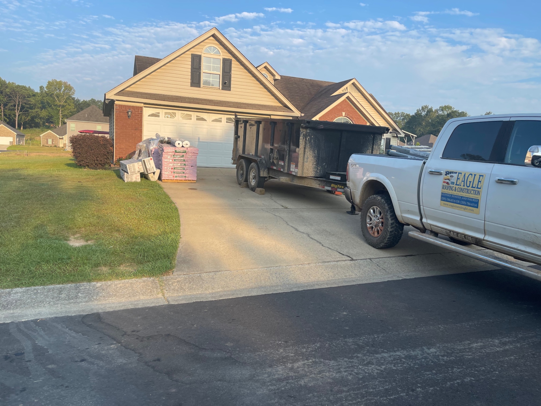 Eagle Roofing truck and trailer parked beside staged roofing materials in a residential driveway before installation