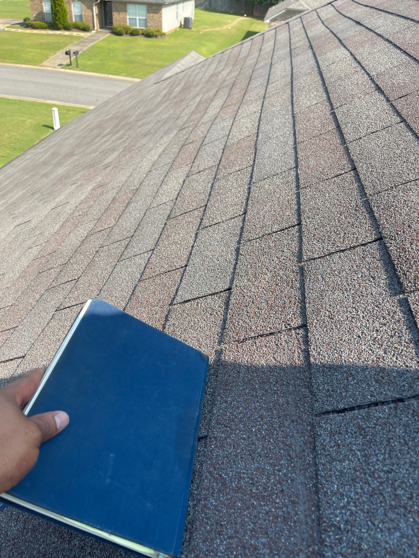 Roof slope inspection view with asphalt shingles and a sample board used for comparison