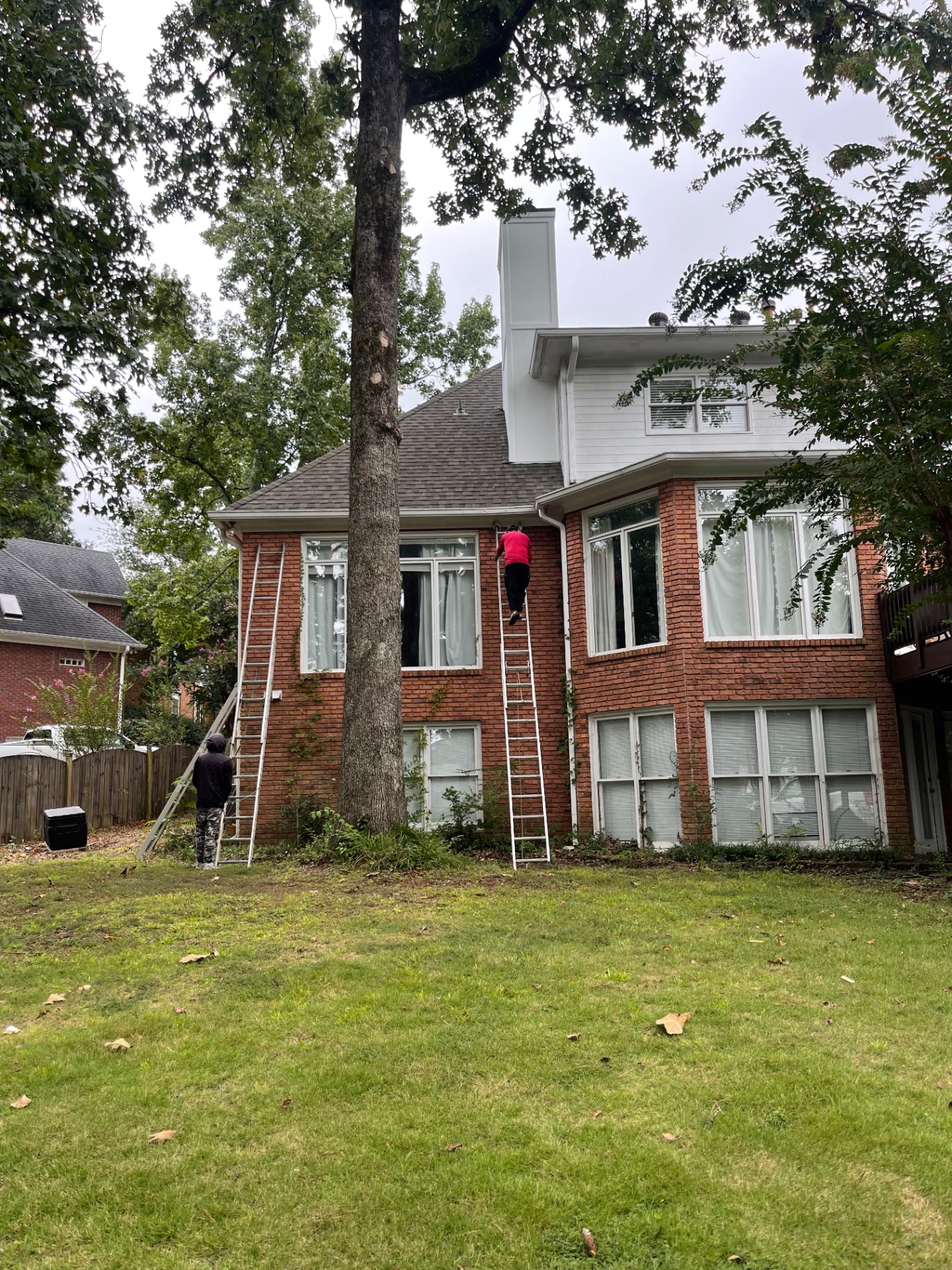 Crew accessing the roof by ladder for chimney repair work on a brick home