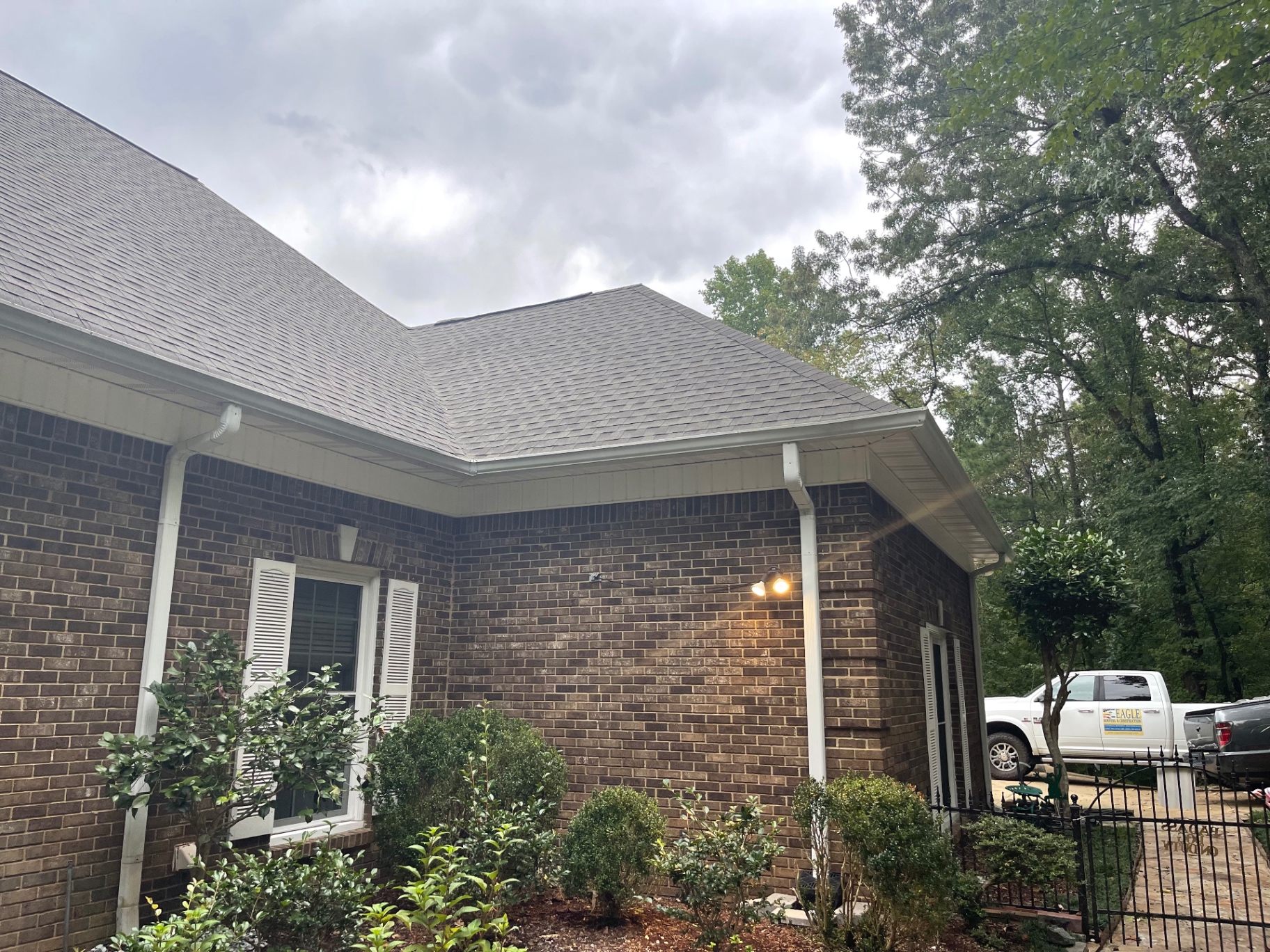 Rear corner view of a brick home with a clean roofline and gutter system after roofing work