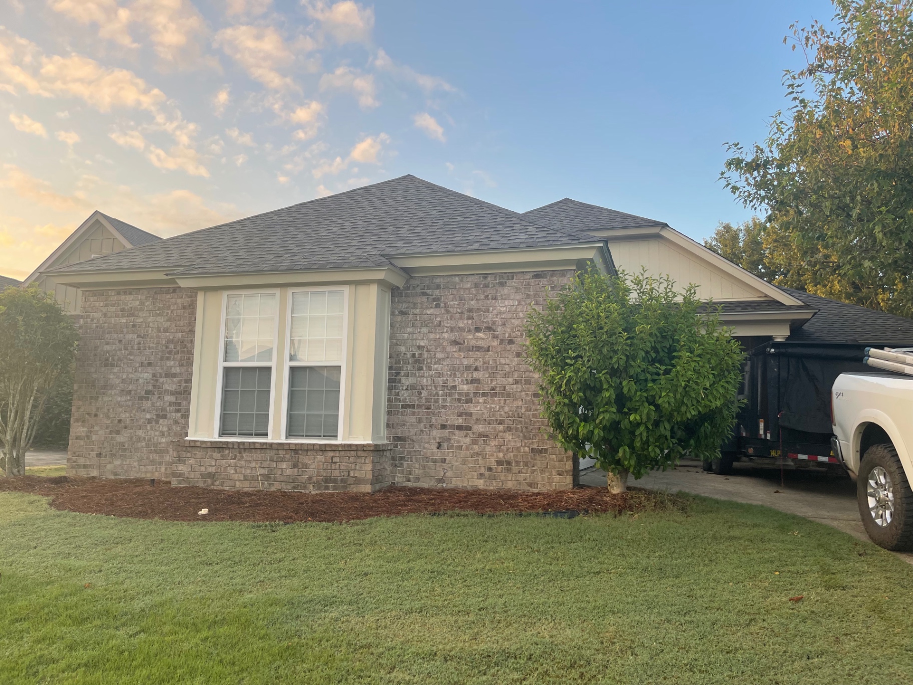 Side elevation of a suburban brick home showing a clean completed shingle roof at golden hour