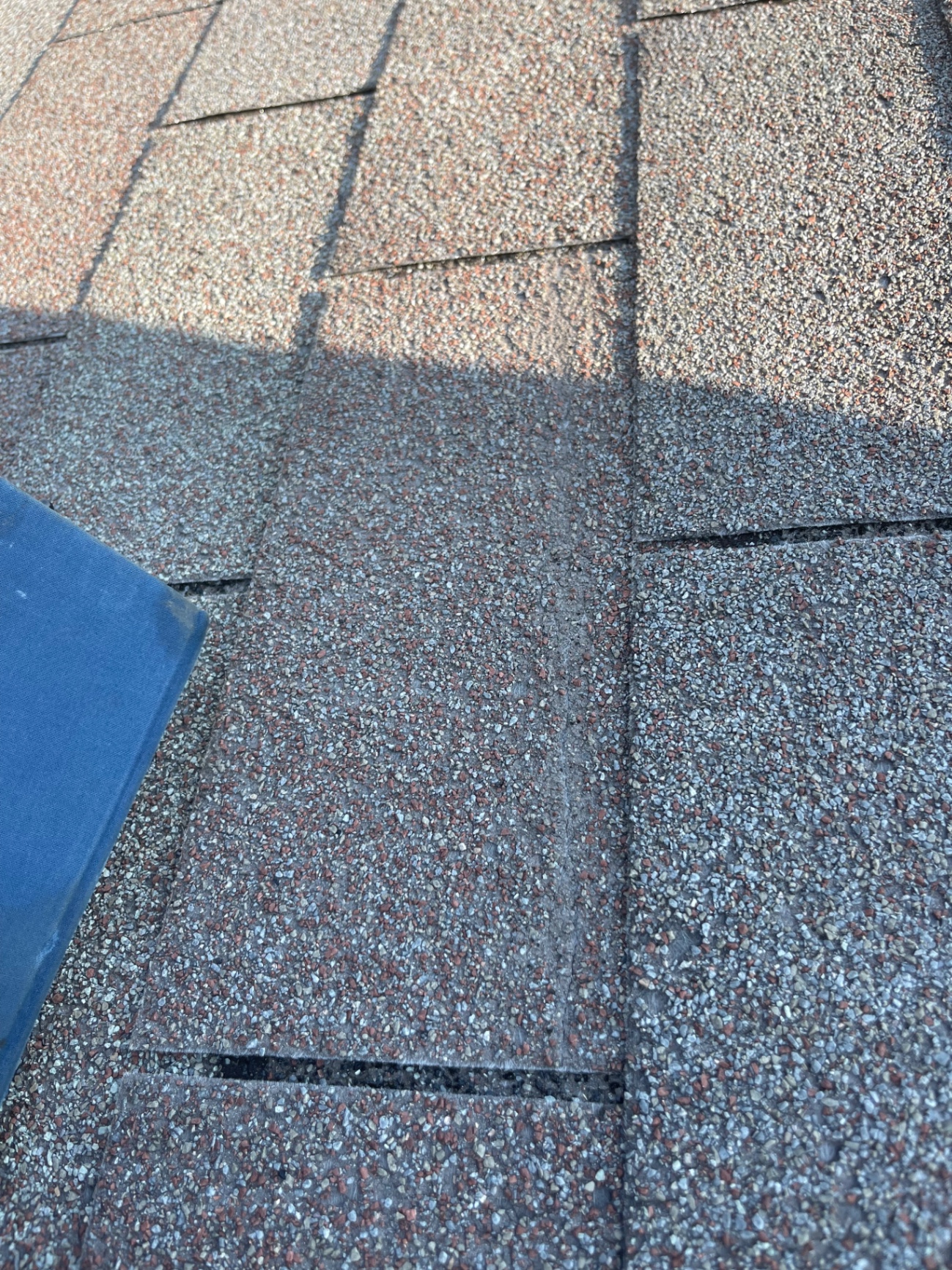 Close-up inspection photo of weathered asphalt shingles showing surface wear and aging