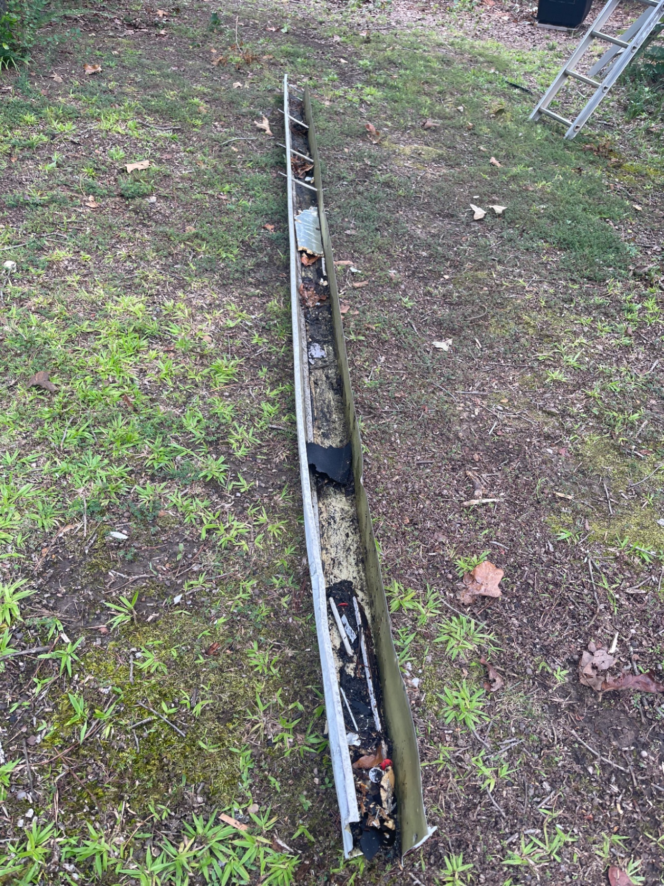Gutter removed from a home showing heavy debris buildup and drainage blockage before repair