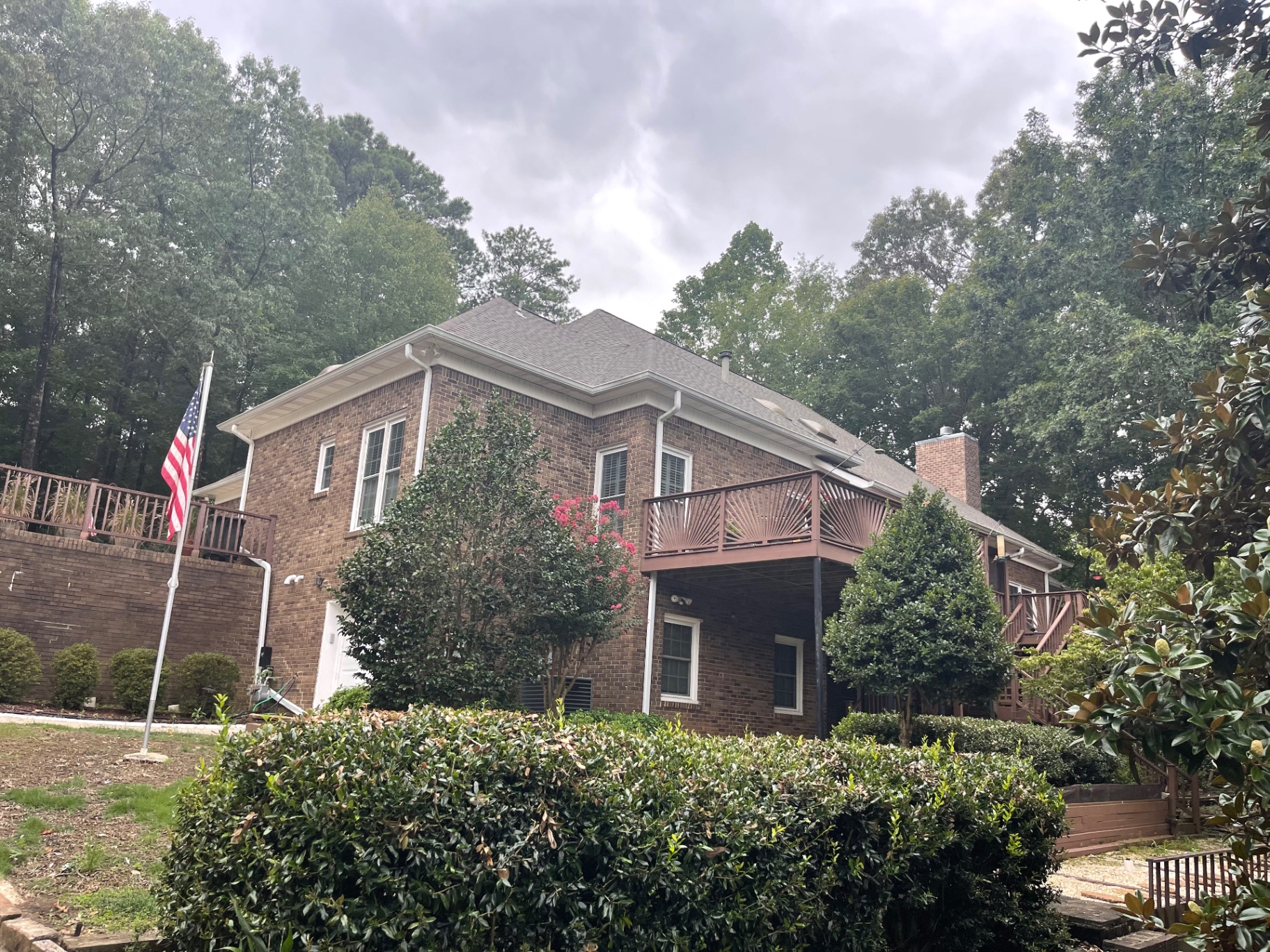 Rear yard elevation of a brick home with elevated deck and completed roofline under storm clouds