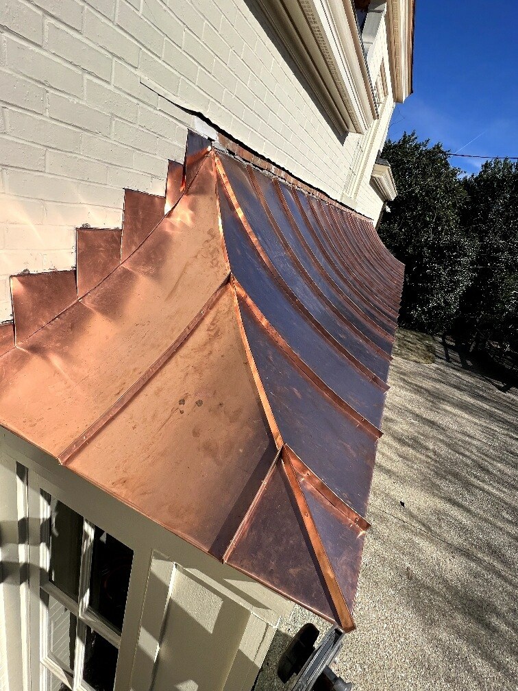 Curved standing seam copper roof with custom step flashing against a white brick wall