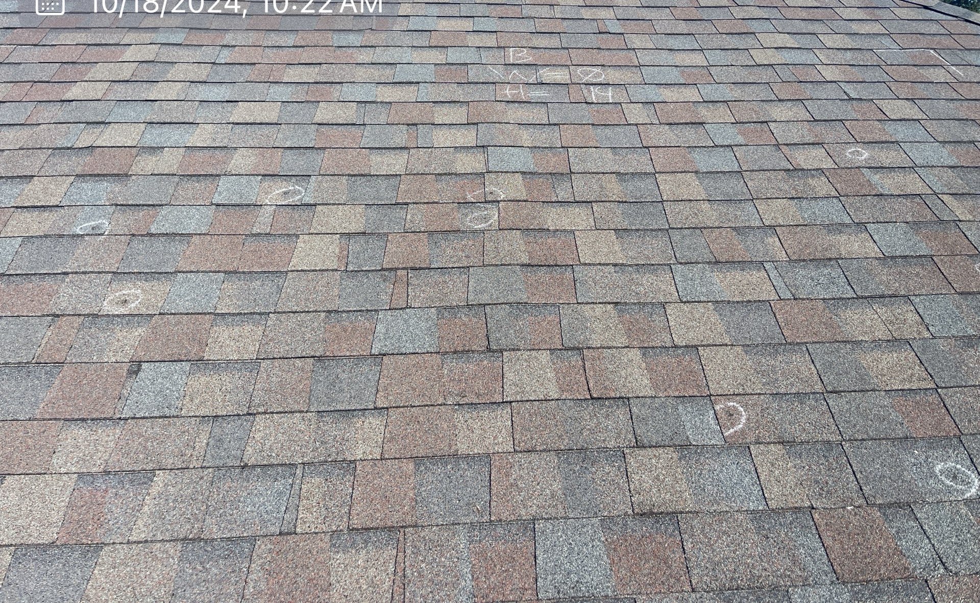 Chalk-marked hail damage on asphalt shingles during a roof inspection