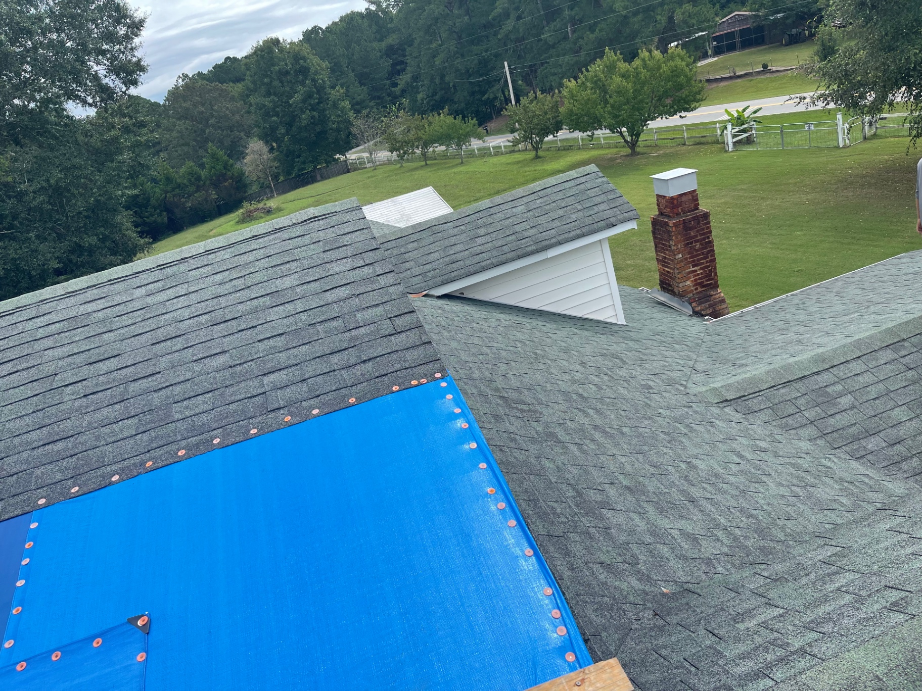 Roof inspection view showing a blue tarp protection area and nearby brick chimney