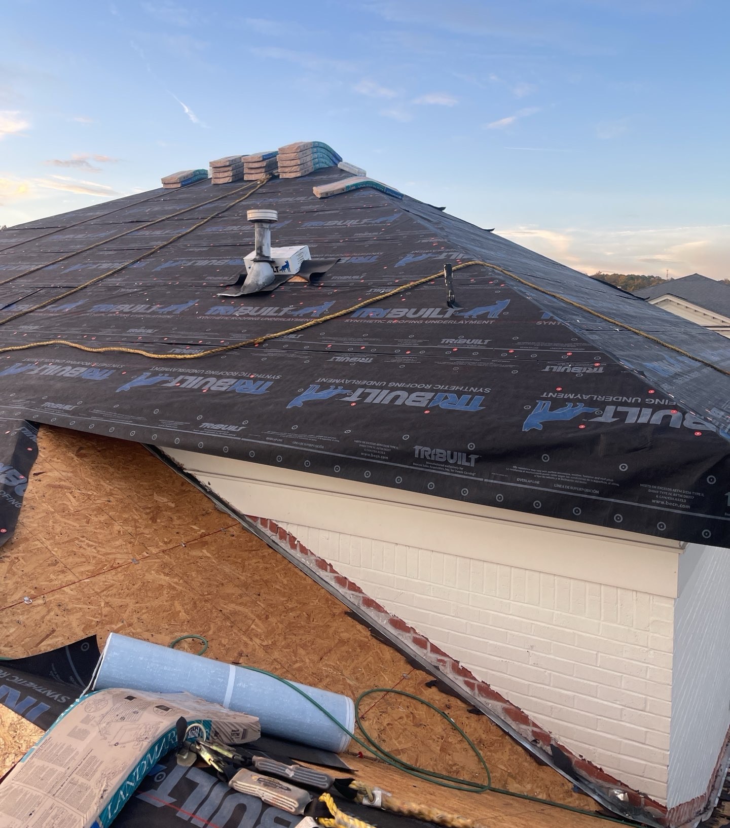 Hip roof covered in synthetic underlayment with staged shingles before final installation