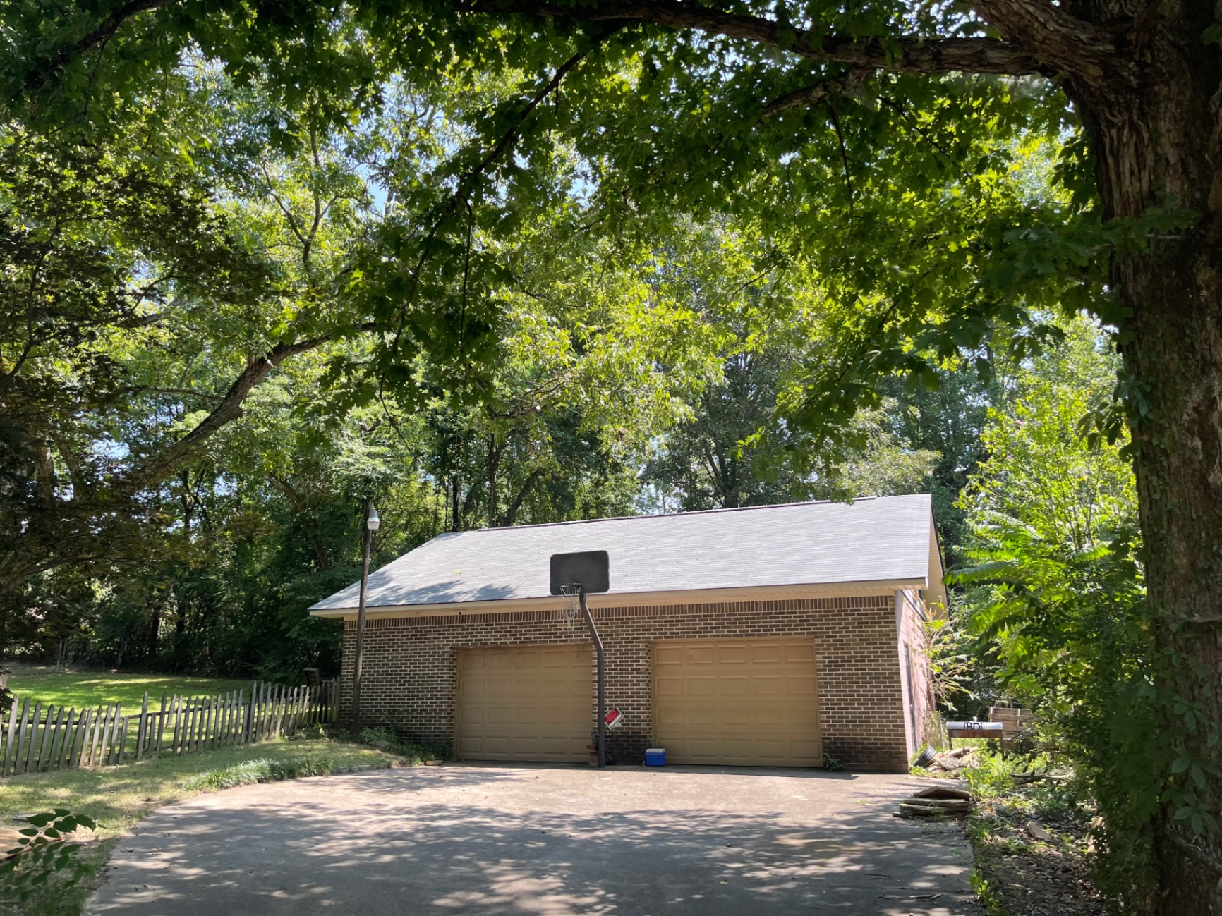 Wide exterior view of a detached brick garage with a completed roof under mature shade trees