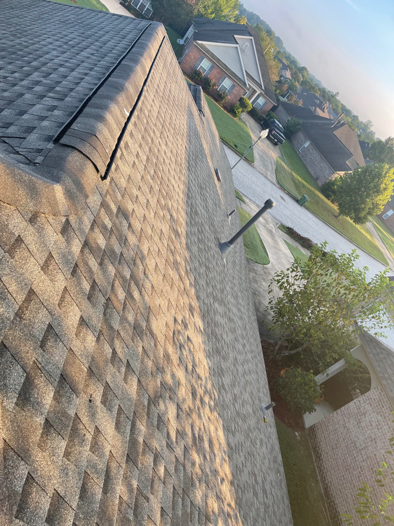 High-angle neighborhood view across a completed roof with ridge vent and pipe penetrations